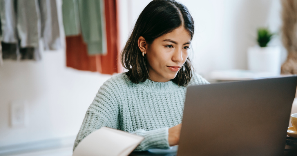 Hispanic woman working remotely on netbook near notebook at home. 